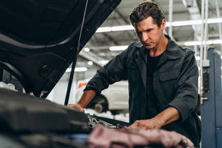 Expertise car mechanic in auto repair service. Caucasian man working attentively. Car maintenance and auto service garage conceptの写真素材