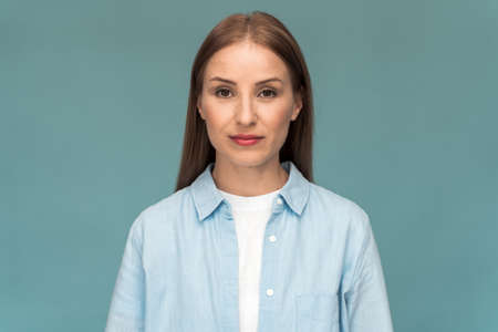Attractive caucasian girl wearing white t shirt and jeans shirt looking straight into the camera. Young woman posing on a blue wall backgroundの写真素材