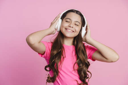 Attractive teenage girl in wireless headphones listens to music, enjoys. Cute little girl having fun on a pink backgroundの写真素材
