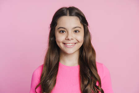 Smiling teenage girl sincerely smiling on a pink background. The girl looks at the cameraの写真素材