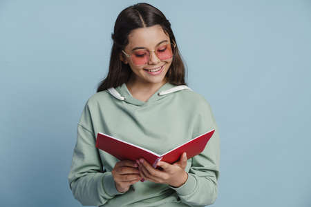 Positive, smiling girl writes something in a notebook. Nice little girl on a blue backgroundの写真素材
