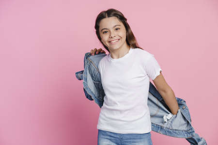 Positive girl wears a denim jacket on a pink background. Girl in casual clothesの写真素材