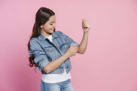 Cute, beautiful teenage girl rolls up the sleeves of a denim jacket. Girl on a pink backgroundの写真素材