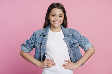 Sincere, charming girl put her hands aside, looking at the camera. Beautiful girl on a pink backgroundの写真素材