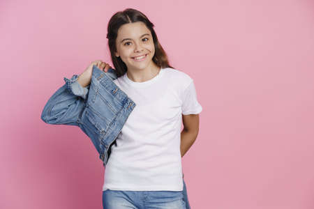 Casual, modern teenage girl wearing a denim jacket. The girl sincerely smiles, looks at the camera on a pink backgroundの写真素材