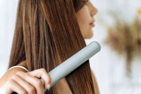 Hairdressing. Woman with beautiful long straight hair using hair straightener. Gorgeous girl straightening healthy hair with flat iron. Hair ironing and hairstyle conceptの写真素材