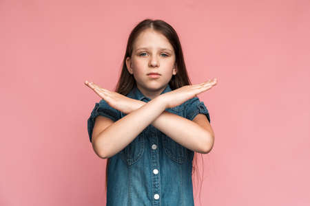Stop, I'm warning. Portrait of angry determined little girl crossing hands and looking at camera with aggression, showing stop gesture, way prohibited. Indoor studio shot pink backgroundの写真素材