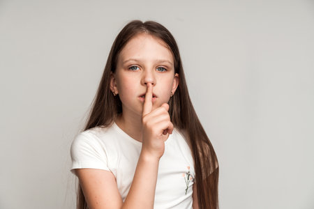 Shh, be quiet! Portrait of funny cute little girl making silence gesture with finger on her lips, keeping some secret, child mystery. Studio shot isolated on white backgroundの写真素材