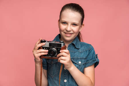 Happy girl posing with vintage photo camera and feeing satisfied. Indoor studio shot isolated on pink backgroundの写真素材