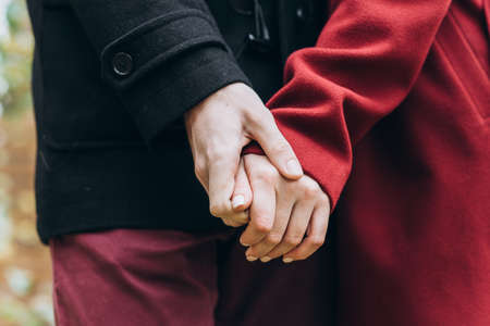 Detail of a young couple in love holding hands and walking through a park on a sunny autumn day. Selective focus. Relationships conceptの写真素材