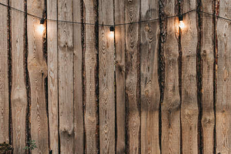 Beautiful yellow light bulbs on the street. Lightbulb hanging at the wooden fence during the autumn evening with light from illuminated. Stock photoの写真素材
