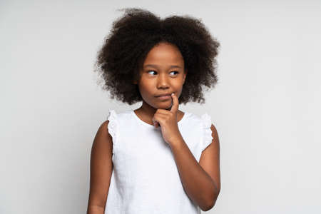 Need to think. Portrait of clever pensive little girl in white shirt pondering solution with serious expression. Child making decision. Studio shot isolated on white backgroundの写真素材