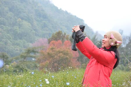 Young happy woman standing in yellow rapeseed field and sukura flower holding a bear dollsの写真素材