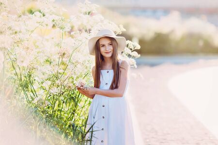 Nice little girl in white dress and hat near giant flowersの写真素材