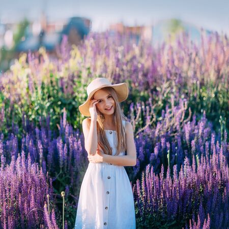 Beautiful little girl in white hat and dress smiling in the parkの写真素材