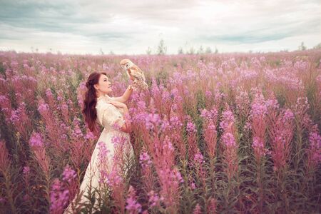 Woman with owl on her hand at beautiful field of pink flowersの写真素材
