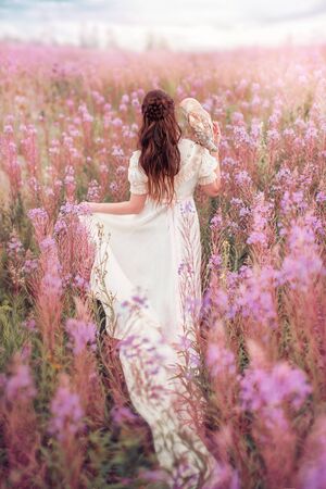 Woman with owl at field of pink flowers.の写真素材