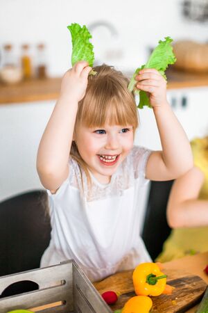 Cute kid, little girl play with salad at kitchen, looking like an Easter bunnyの写真素材