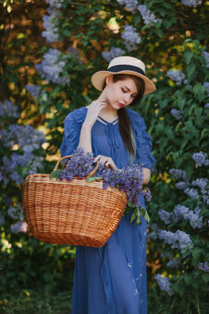 Young beautiful girl with a basket full of lilac flowers in a blooming gardenの写真素材