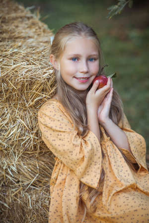 Nice smiling girl with blue eyes and long blonde hair gently holds an apple near her cheekの写真素材