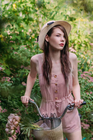 Beautiful stylish girl in retro hat walks with bicycle in gardenの写真素材