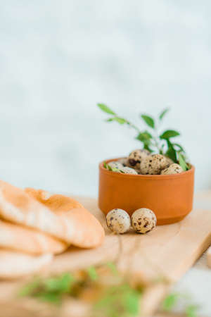 Quail eggs in a bowl with bread and herbs as an Easter decor on a wooden table in bright room.の写真素材