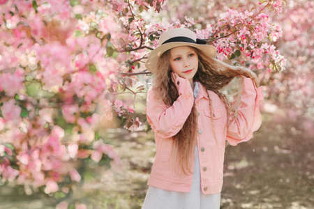 Beautiful spring dreaming scene with beautiful young girl with long blonde wavy hair in apple blooming pink garden. Horizontal picture.の写真素材