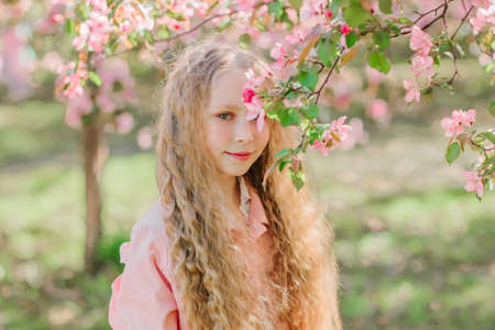 Longhaired stylish blonde girl looking throw bloom apple branches with pink colored big flowers. Dreamy picture. Horizontal photoの写真素材