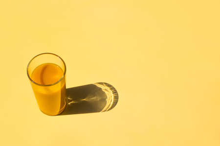 One glass with yellow colorful mango fresh juice stay on yellow table. Minimalistic trendy background with copy space.の写真素材
