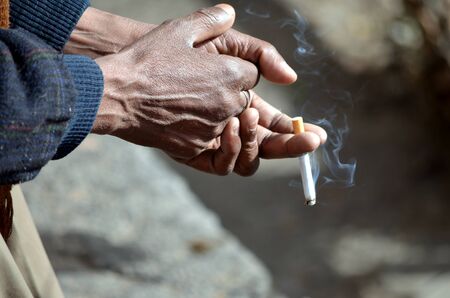 Old and dusty hands holding recently lit cigaretteの写真素材