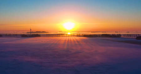 winter sunrise landscape in Sneek, Friesland The Netherlands. Ariel view of Frozen lake with sunset and birds in flight. Birds eye view of Beautiful sunset over snow on cold and windy winter dayの写真素材