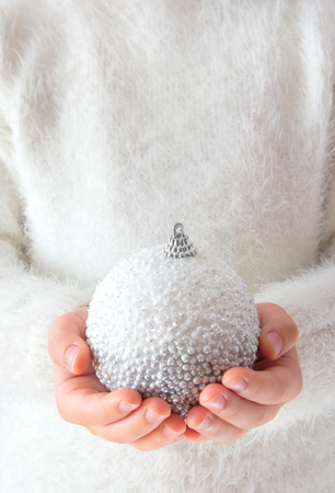 little girl in white sweater holding a Christmas ballの写真素材