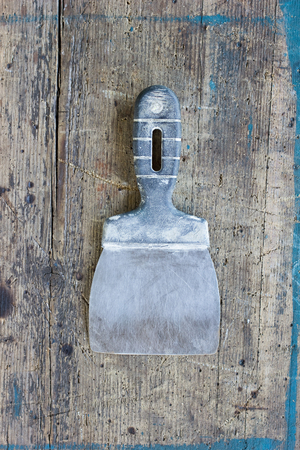 Old, dirty putty knife against wooden plank. Tool series.