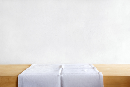 Rustic table with white table linen against grunge cement wall. Vintage background template, product display montage.の写真素材