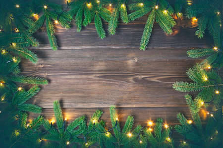 Christmas decoration. Fir tree and christmas lights frame on rustic, wooden background. High angle view.の写真素材