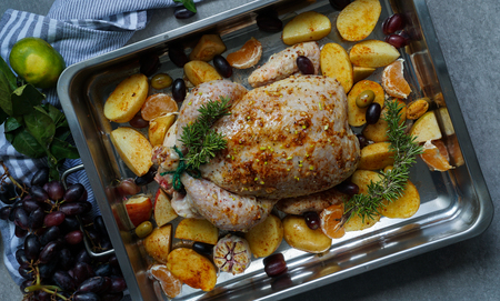 Baked turkey or juicy chicken with golden crispy skin with grapes and potatoes, tangerine. Roasted chicken in baking dish. Christmas dinner. Flat lay. Top viewの写真素材