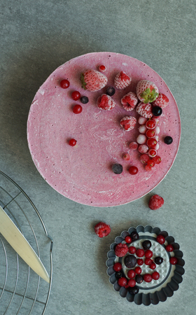 Vegan raw cake with berries, cashew cream, coconut butter and coconut milk, and base made of almonds, dates and dried apricots, oat flakes, lyophilisated berry, top view, stone grey backgroundの写真素材