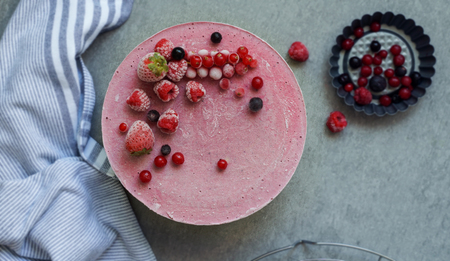 Vegan raw cake with berries, cashew cream, coconut butter and coconut milk, and base made of almonds, dates and dried apricots, oat flakes, lyophilisated berry, top view, stone grey backgroundの写真素材