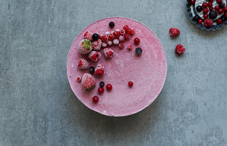 Vegan raw cake with berries, cashew cream, coconut butter and coconut milk, and base made of almonds, dates and dried apricots, oat flakes, lyophilisated berry, top view, stone grey backgroundの写真素材