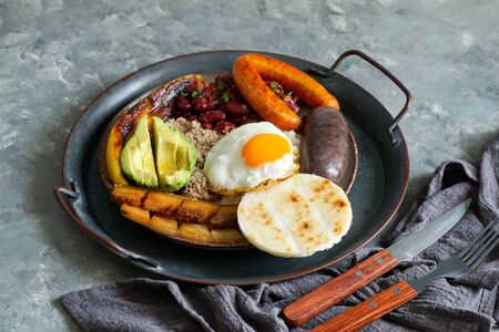 Colombian food. Bandeja paisa, typical dish at the Antioquia region of Colombia - chicharrÃ³n (fried pork belly), black pudding, sausage, arepa, beans, fried plantain, avocado egg, and rice.の写真素材