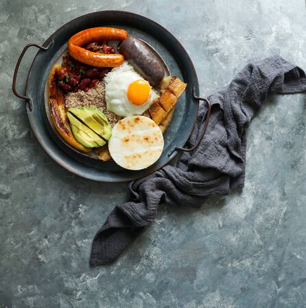 Colombian food. Bandeja paisa, typical dish at the Antioquia region of Colombia - chicharrÃ³n (fried pork belly), black pudding, sausage, arepa, beans, fried plantain, avocado egg, and rice.の写真素材