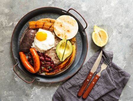 Colombian food. Bandeja paisa, typical dish at the Antioquia region of Colombia - chicharrÃ³n (fried pork belly), black pudding, sausage, arepa, beans, fried plantain, avocado egg, and rice.の写真素材