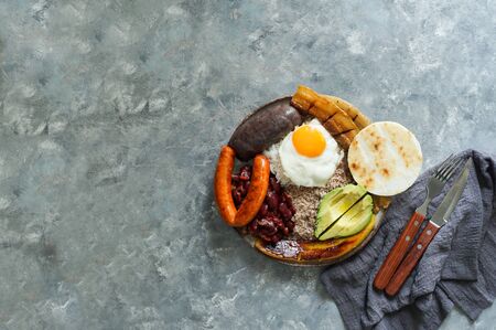 Colombian food. Bandeja paisa, typical dish at the Antioquia region of Colombia - chicharrÃ³n (fried pork belly), black pudding, sausage, arepa, beans, fried plantain, avocado egg, and rice.の写真素材