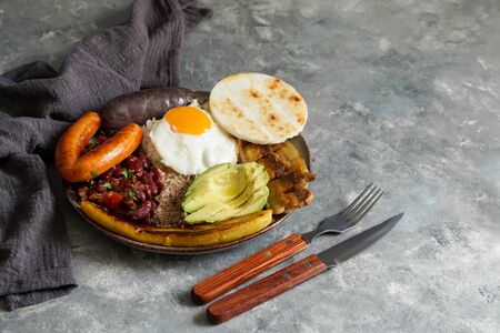 Colombian food. Bandeja paisa, typical dish at the Antioquia region of Colombia - chicharrÃ³n (fried pork belly), black pudding, sausage, arepa, beans, fried plantain, avocado egg, and rice.の写真素材