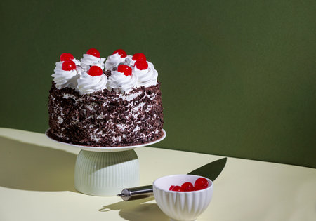 Chocolate cake with cherries on a white stand on a green background