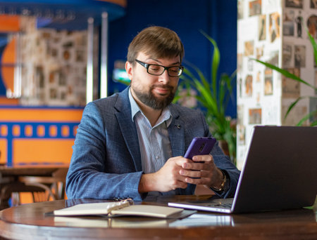 Photo of happy young businessman using laptop computer and talking on smartphone