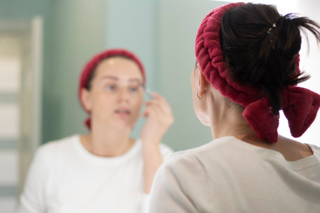Woman applies makeup looking in the mirror, paints her eyebrows with a pencilの写真素材