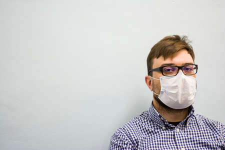 Portrait of a young man in glasses in a medical protective mask for a face on a light background and looking at the cameraの写真素材