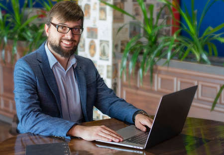 Young man with beard sitting at the table and using laptopの写真素材