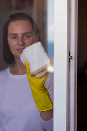Service cleaning young smiling positive woman in white washes the windows of a white rag girlの写真素材